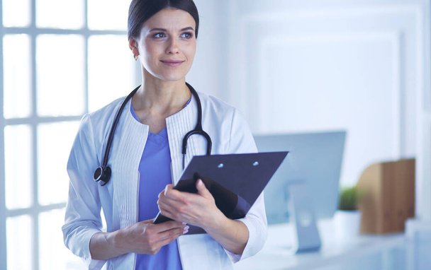 Young smiling female doctor with stethoscope holding a folder at doctors office - Photo, Image