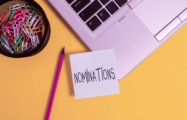 Handwriting text writing Nominations. Concept meaning the act of officially suggesting someone for a job or position Metallic laptop sticky note clips container pencil colored background. - Photo, Image