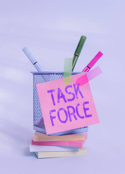Text sign showing Task Force. Conceptual photo a group of showing who are brought together to do a particular job Sticky note arrow banners stacked pads metal pens holder pastel background. - Foto, afbeelding
