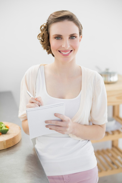 Jeune femme debout dans sa cuisine écrivant une liste de courses
 - Photo, image