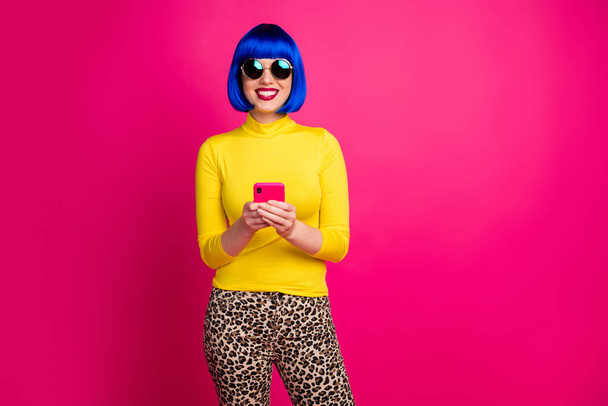 Photo of beautiful lady hold telephone chatting friends good mood wear trendy specs yellow turtleneck blue bob wig leopard pants isolated vivid shine pink color background - Photo, image