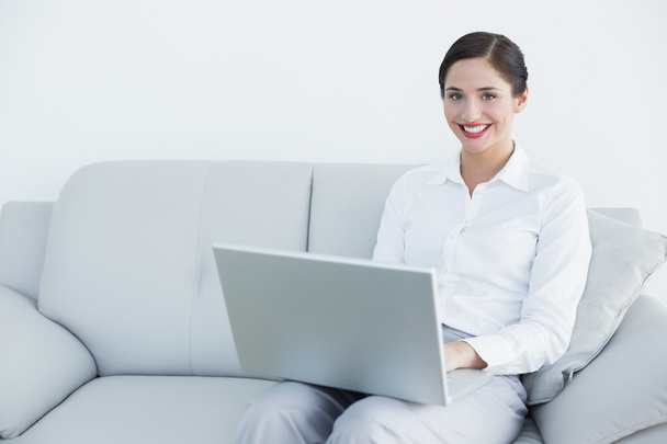Smiling well dressed young woman using laptop on sofa - Foto, Imagem