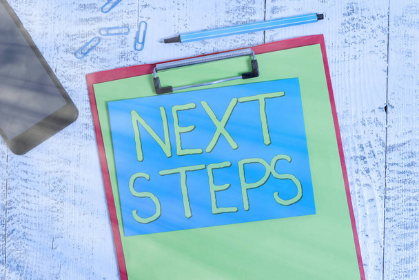 Writing note showing Next Steps. Business photo showcasing something you do or plan after you ve finished something else Clipboard paper sheet marker note clips smartphone wooden background. - Photo, Image