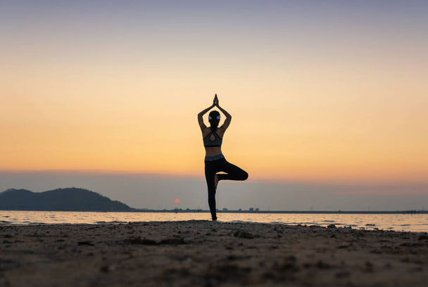 nő gyakorló jóga közben szürreális naplemente a tengerparton. egészséges koncepció és edzés. - Fotó, kép