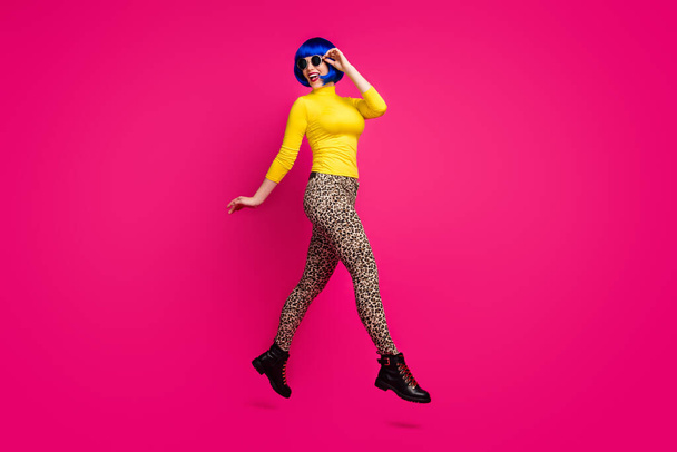 Full length profile photo of cheerful lady jumping high walk street cool traveler wear specs yellow turtleneck blue short wig boots leopard pants isolated bright pink color background - Foto, Imagem