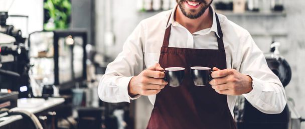 Πορτρέτο του όμορφου μουσάτο μπάρμαν μικρών επιχειρήσεων που χαμογελά και κρατώντας ένα φλιτζάνι καφέ στο καφέ ή καφετέρια. Αρσενικός μπάρμαν στέκεται στο καφέ - Φωτογραφία, εικόνα