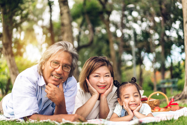 Portrait des glücklichen Großvaters mit Großmutter und kleines nettes Mädchen genießen entspannen Blick auf camara im Sommerpark.Junge Mädchen mit ihren lachenden Großeltern zusammen lächeln.Familie und Zweisamkeit - Foto, Bild