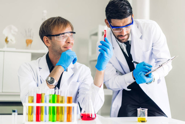 Ammattimainen kaksi tiedemies mies tutkimus ja työskentely tekee kemiallisen kokeen tehdessään analysointi ja sekoittaminen nestettä koeputkessa. - Valokuva, kuva