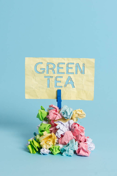 手書きのテキストは緑茶を書きます。椿の葉や芽から作られるお茶の概念意味メモ山色の砕いた紙の布ピンリマインダー青の背景. - 写真・画像