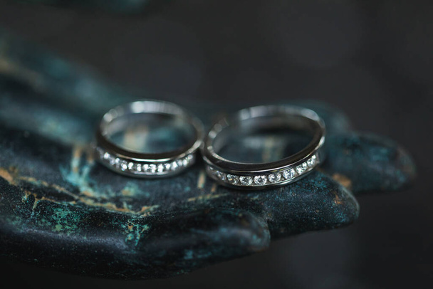 Due anelli da sposa in oro bianco con diamanti sulla mano di Buddha in metallo su sfondo scuro. Concetto di amore spirituale
. - Foto, immagini