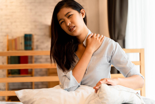 Portrait of 20s young Asian woman having pain in her neck and back in bedroom at night. Cervical arthritis, osteochondrosis, diseases of musculoskeletal system - Foto, immagini