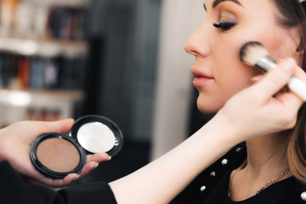 escova de pó na mão de um artista de maquiagem perto de um rosto de mulher em um salão de beleza profissional
 - Foto, Imagem