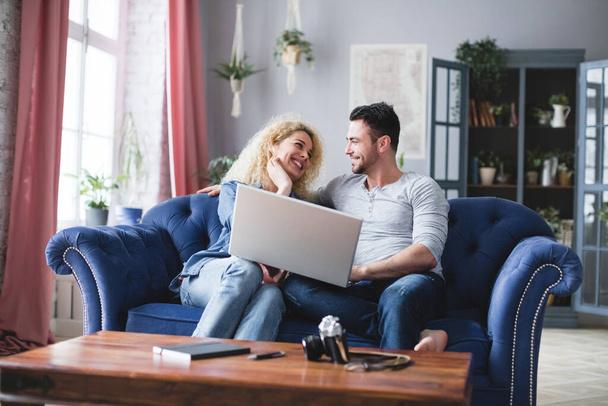 Happy couple using laptop on sofa at home. Choose online. - Foto, imagen