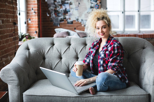 Young beautiful woman on the sofa with laptop and coffee.  Web surfing. - Foto, imagen