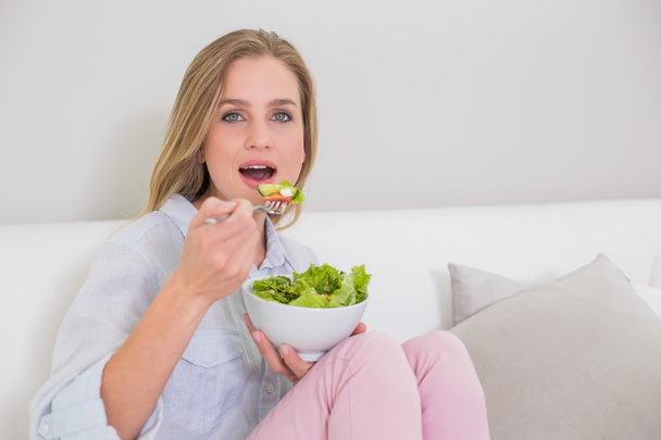 Surprised casual blonde sitting on couch eating salad - Photo, image