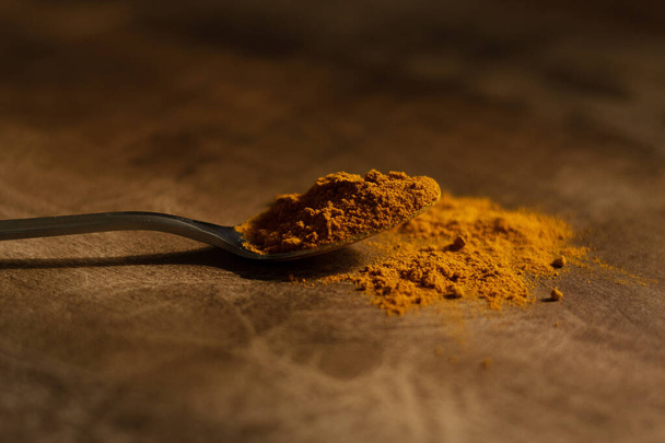 A spoonful of turmeric powder in a metal spoon. Dark wood background in warm shades. - Foto, Imagen