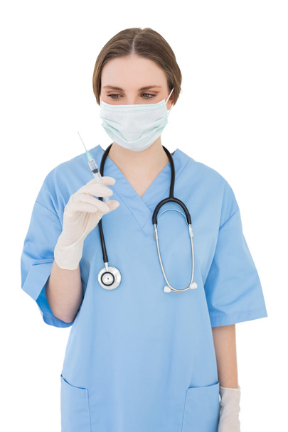 Женщина-врач держит укол и смотрит на него на белом фоне
 - Фото, изображение