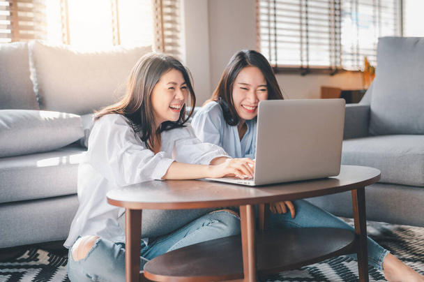 Dvě šťastné asijské ženy nejlepší přátelé v příležitostném oblečení smích při práci s notebookem doma v obývacím pokoji - Fotografie, Obrázek