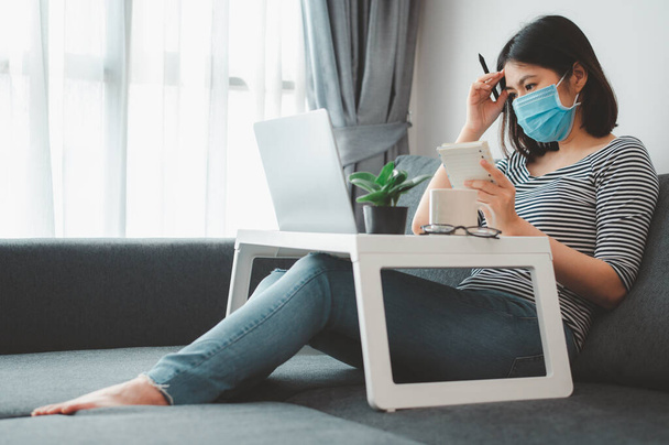 Asian woman wearing face mask working from home during coronavirus quarantine - 写真・画像