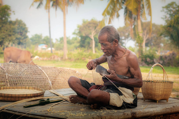 Oturan yaşlı adam tarladaki çöp yığınında duran bambu tavuklarıdır.. - Fotoğraf, Görsel