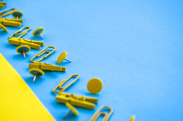 Office supplies in the form of colored buttons and paper clips, clothepins on yellow and blue background, copy space, border and frame, back to school concept of office chancery - Foto, imagen