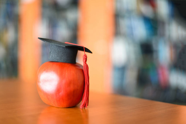 Educazione concetto di apprendimento / Graduation cap sulla mela sul tavolo con libreria sullo sfondo
 - Foto, immagini