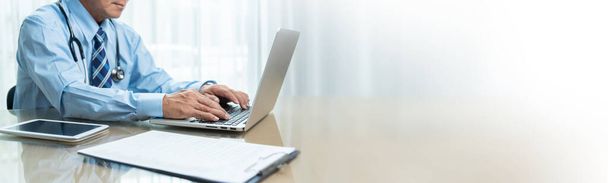 Азіатський старший Доктор використовує ноутбук, цифрову планшет і дошку для настільних комп'ютерів у медичній кімнаті. Лікар у синій сорочці сидить на роботі в лікарні. Banner, Web, Panoramic, Copy space. - Фото, зображення