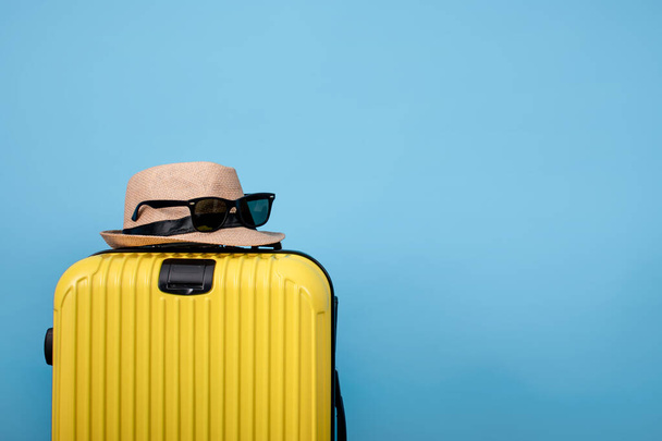 Primer plano de la maleta amarilla con sombrero y gafas de sol en la bolsa sobre un fondo azul
 - Foto, imagen