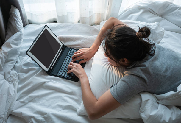 Mujer asiática acostada en la cama y utilizando el ordenador portátil
. - Foto, imagen