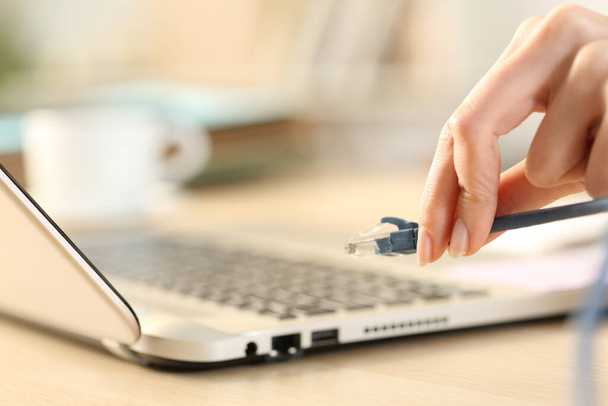 close-up van vrouw handen pluggen ethernet kabel op laptop op een bureau - Foto, afbeelding