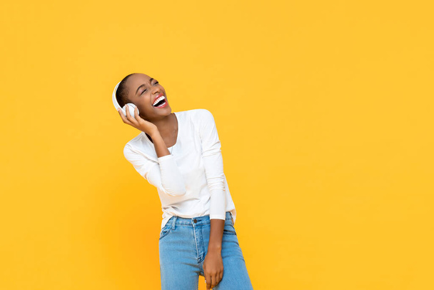Heureuse femme afro-américaine riant tout en écoutant de la musique sur casque sans fil isolé sur fond jaune
 - Photo, image