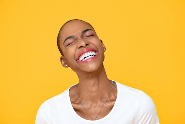 Heureuse femme afro-américaine optimiste riant avec les yeux fermés isolé sur fond jaune coloré
 - Photo, image