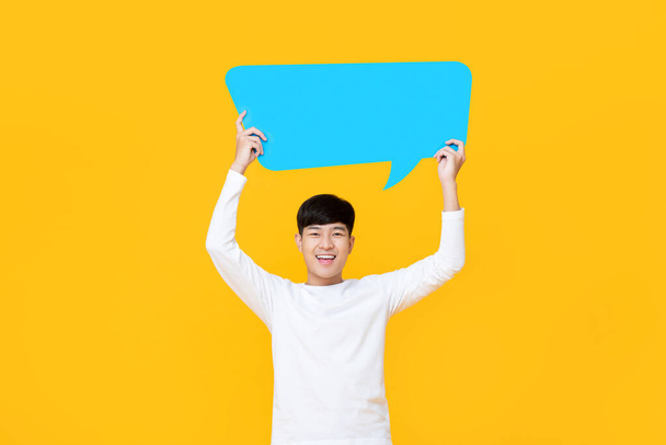 Eccitato sorridente giovane carino uomo asiatico che tiene la bolla discorso blu con spazio vuoto per il testo su sfondo giallo colorato
 - Foto, immagini