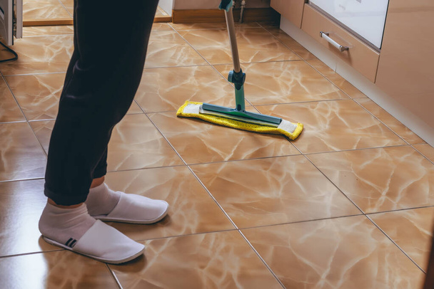 Жінка миє підлогу з плитки на кухні мопедом. прибирання квартири. чистий ключ до успіху. жовта ганчірка
. - Фото, зображення