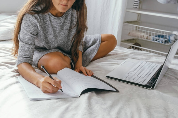 woman sitting on the bed in the bedroom at home and make notes using laptop - Foto, imagen