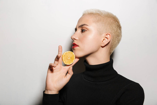 Portrait of an attractive young blonde short haired woman posing with halved lemon isolated over white background - Φωτογραφία, εικόνα