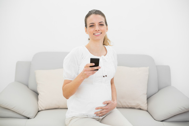 Cute pregnant woman holding her smartphone smiling happily at camera - Fotó, kép