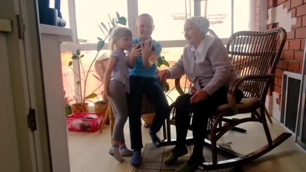 grandchildren teach 80 year old grandmother to work on a smartphone. playing with a smartphone. Make purchases online. are photographed. on the veranda of the house. Communicate on the Internet - Кадри, відео