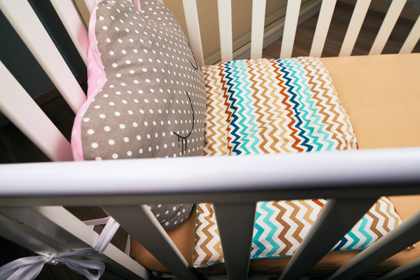 Λευκή κούνια μωρού με ένα χαριτωμένο καφέ ροζ μαξιλάρι με ένα κουτάκι. καφέ στρώμα. Άνετο κρεβάτι για το μωρό. φωτογραφία θέματος - Φωτογραφία, εικόνα