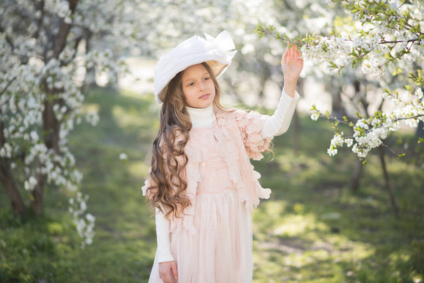 little girl wearing pink dress and retro hat in the spring garden - 写真・画像