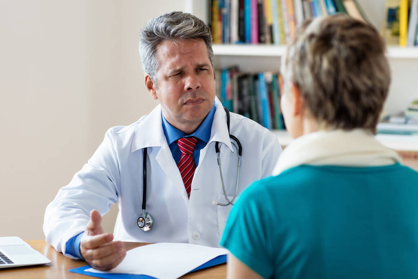 Sensitive mature doctor listening to patient with pain and corona symptoms at hospital - Photo, image