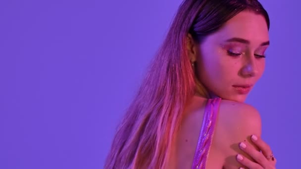 A side view of charming gorgeous woman with fashion glitter makeup is posing while doing a silence gesture isolated over violet neon background - Séquence, vidéo