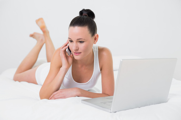 Casual woman using cellphone and laptop in bed - Фото, зображення
