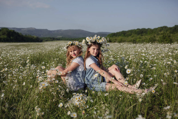 twee schattige tienermeisjes in denim overall lopen in een madeliefje veld. idee en concept van gezondheid, gelukkige jeugd, vriendschap - Foto, afbeelding