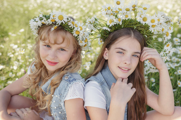 dwie słodkie nastolatki dziewczyny w dżinsowych ogrodniczkach chodzić w stokrotki pole. idea i koncepcja zdrowia, szczęśliwe dzieciństwo, przyjaźń - Zdjęcie, obraz