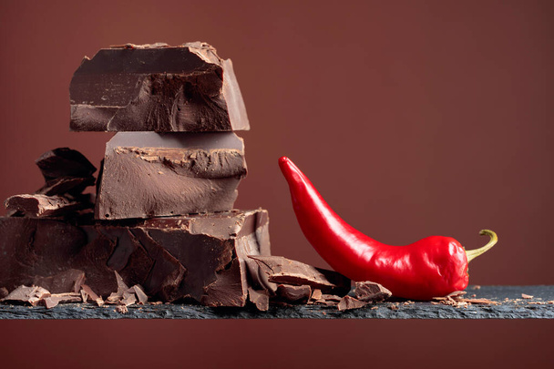 Кусочки черного шоколада с красным перцем на коричневом фоне. Копирование пространства
. - Фото, изображение
