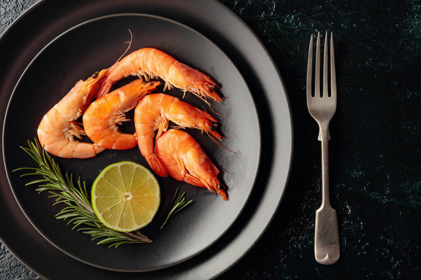 Vařené krevety s rozmarýnem a citrónem na černém talíři. Horní pohled. - Fotografie, Obrázek