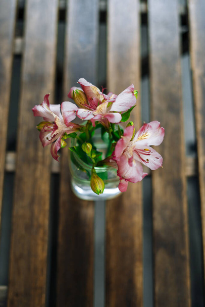 Prachtige alstroemeria in vaas op houten tafel in zomercafé. Zacht zomers boeket in een glazen vaas. Roze bloemen op een zonnige dag. - Foto, afbeelding