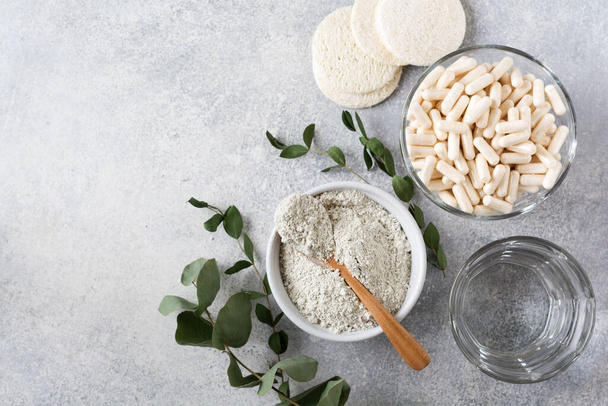 Closeup collagen for preparing a cosmetic mask in ceramic bowl with spoon and capsules for diet food, loofah sponges and dry eucalyptus branches on old gray concrete background. Flat lay with copy space. - Photo, image