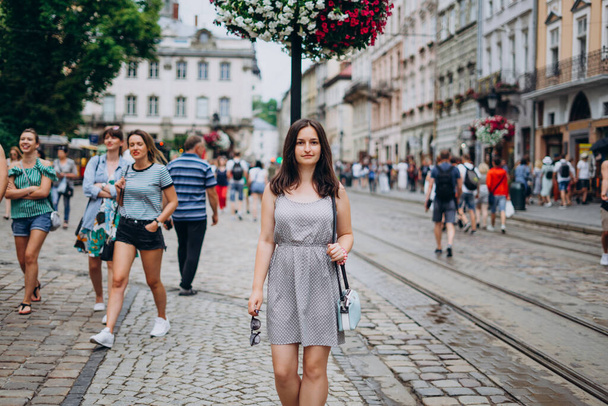 Beautiful girl in a summer dress walks the city. Brunette girl in a sundress with a handbag and glasses. Girl on the background of the city. - Photo, Image